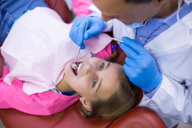 Dentist examining young patient with dental tools in a clinic. Ideal for use in healthcare, dental care, pediatric dentistry, and medical treatment contexts. Suitable for illustrating dental checkups, oral health, and professional dental services.