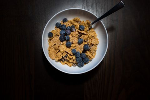 Overhead breakfast bowl featuring whole grain flakes topping fresh blueberries and spoon