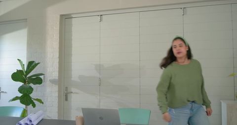 Asian woman walking past workspace with laptop and blueprints in modern studio