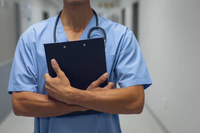 This image shows a male surgeon holding a clipboard in a hospital corridor. It can be used for healthcare-related content, medical articles, hospital brochures, and promotional materials for medical services. The image highlights professionalism and readiness in a clinical setting.