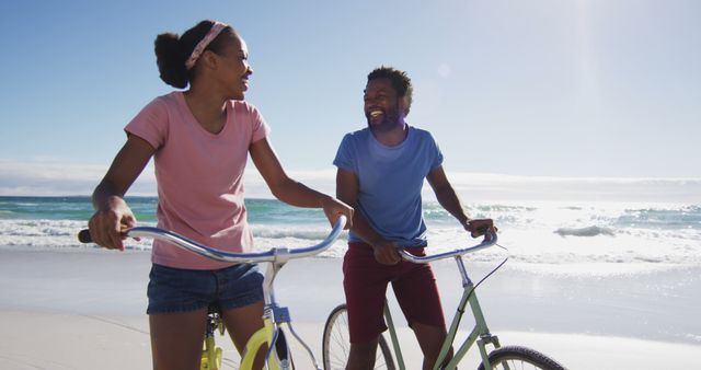 African american couple smiling and riding bikes on the beach. healthy outdoor leisure time by the sea.