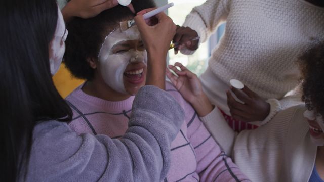 A group of diverse friends are applying face masks on each other, creating a relaxed and joyful atmosphere. They are laughing and enjoying quality time together, highlighting a theme of friendship and self-care. This image can be used for promoting skincare products, beauty salons, or articles about friendship and wellness activities.