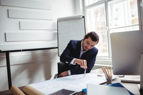 Architect Measuring Blueprints Using Compass Office Environment
