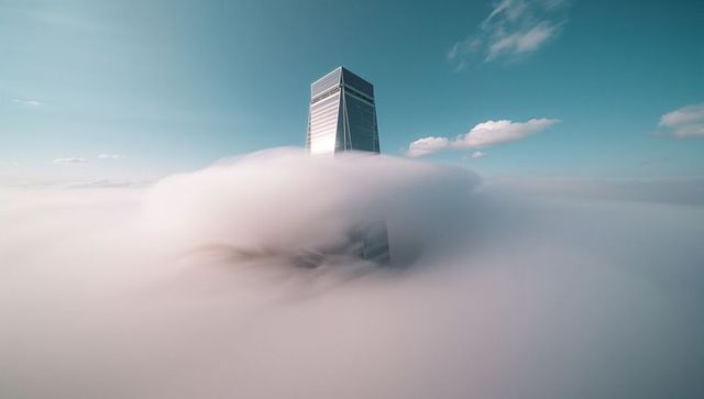 Skyscraper emerging through dense fog in serene sky