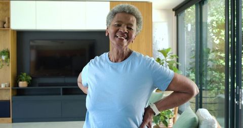Senior african american woman smiling in modern living room wearing smartwatch, light blue tee