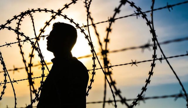Silhouette man behind coiled razor wire at sunrise conveying isolation and security risk