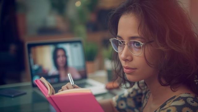 Focused woman taking notes in home office during remote work