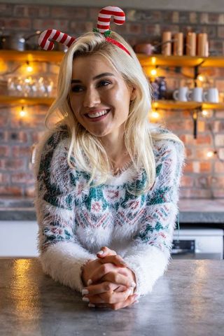 Smiling woman leaning on counter wearing candy-cane headband and fuzzy christmas sweater