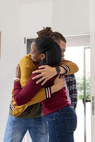 Multiracial couple embracing in sunlit entryway showing rings and smartwatches