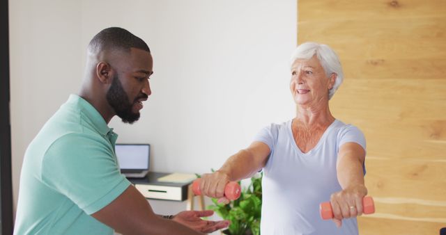 Senior woman lifting dumbbells with assistance from personal trainer. Perfect for articles on senior fitness, personal training, active aging, and health promotions. Useful for illustrating exercise regimens for older adults or advertising fitness coaching services.