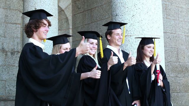 Group of graduates giving thumbs up while standing in front of university building. Celebrating their successful graduation and achievements. Useful for educational success themes, student-focused advertisements, and academic achievement promotions.