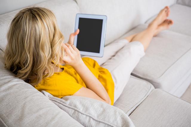 Woman talking on mobile phone while using digital tablet in living room at home