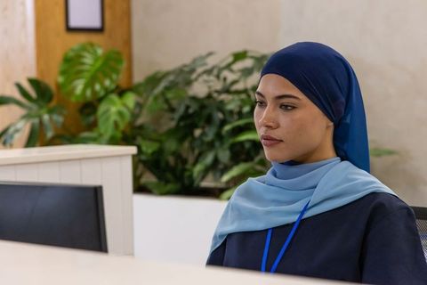 African american receptionist wearing navy hijab and id badge at modern office desk