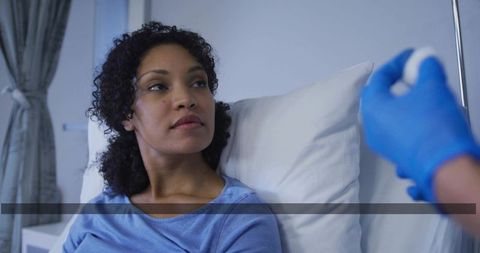 Patient receiving injection from gloved healthcare clinician while resting in hospital bed