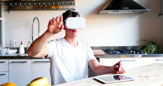 Man wearing VR headset in modern kitchen, engaging with virtual reality technology. Suitable for illustrating usage of VR in everyday life, modern technology, and innovative kitchen designs.