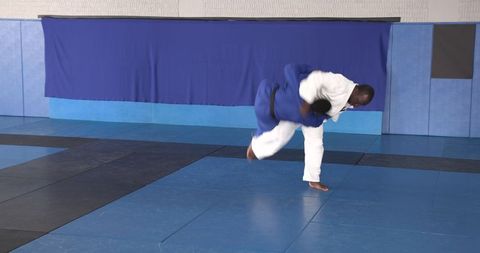 Martial artists executing judo throw on tatami mats