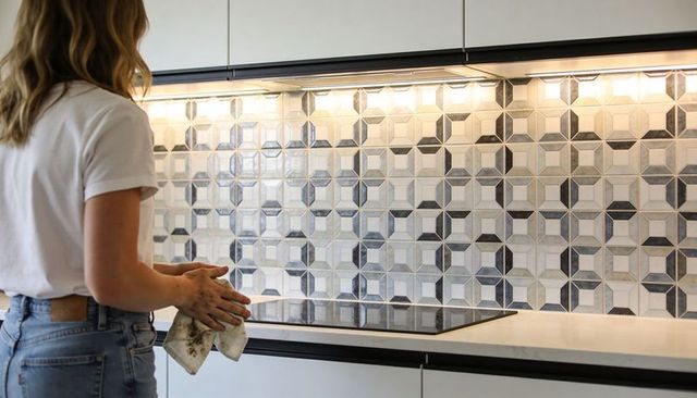 Woman wiping modern geometric tile backsplash and induction cooktop in minimal kitchen