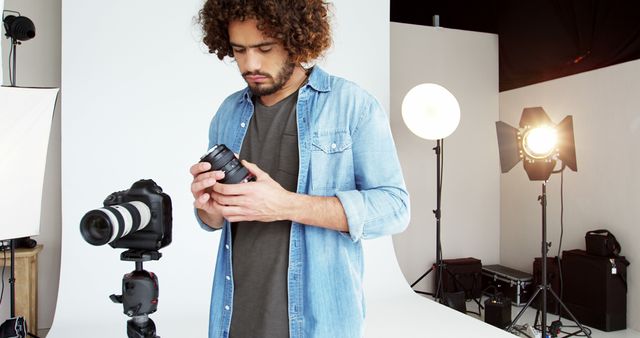 A young Caucasian male photographer is checking his camera equipment in a professional studio setup, with copy space. His focused expression and the array of lighting equipment around him suggest a meticulous preparation for a photo shoot.