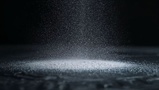 Falling powder particles forming illuminated pile on dark surface with spotlight