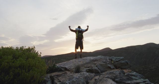 Caucasian male survivalist with arms in the air, celebrating reaching mountain peak in wilderness. exploration, travel and adventure, survivalist in nature.