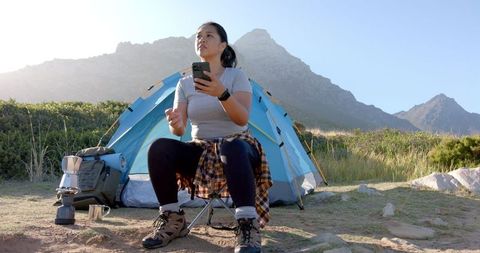 Woman Relaxing by Mountain Tent Using Smartphone During Camping Adventure