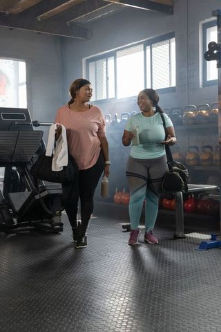 African american women walking through industrial gym after workout holding water bottles