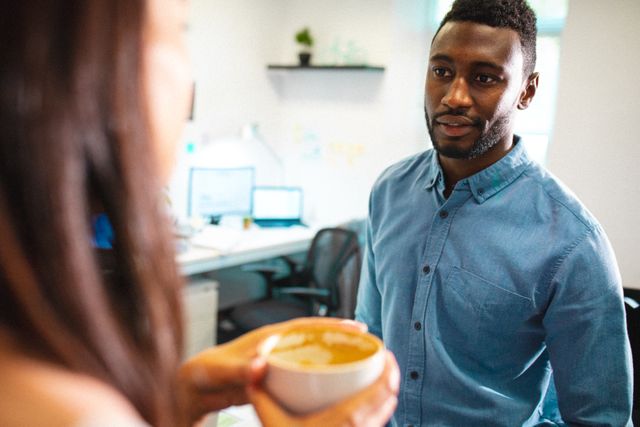 African american businessman talking with female colleague having coffee in creative office. creative business and modern office.