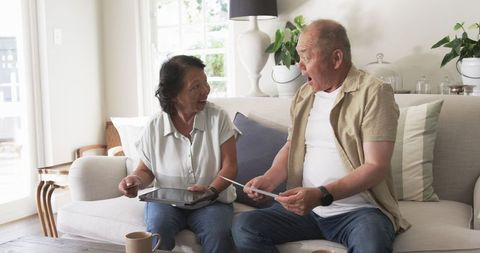 Joyful Senior Couple Reading Letters at Home with Digital Tablet and Mug