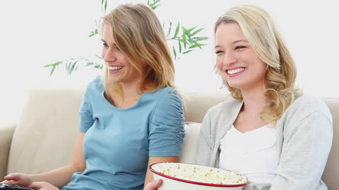 Smiling friends watching TV enjoying popcorn on cozy couch