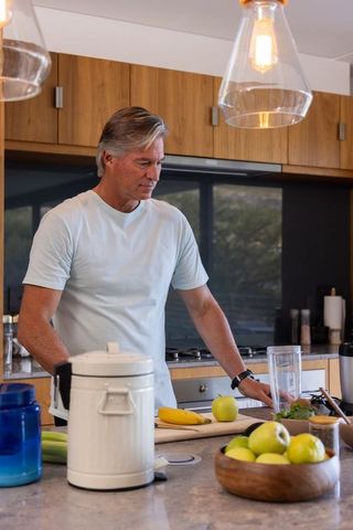 Mature man preparing healthy smoothie at modern kitchen island, minimalist daily lifestyle