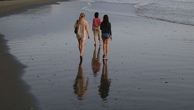 Three women walking along wet beach leaving reflections and footprints