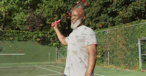 Senior Man in Vibrant Polo Shirt Playing Tennis Outdoors with Red Racket