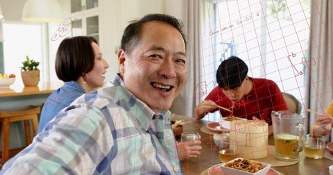 Smiling man raising glass at family dinner sharing noodles and conversation in home kitchen