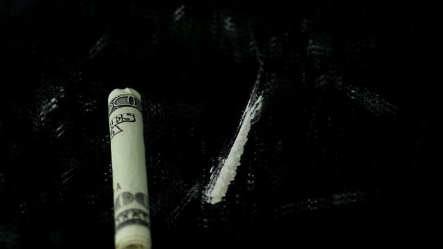 Depicting drug use through a close-up video of a rolled dollar bill alongside a line of cocaine on a black background. This might be used in articles or presentations about drug addiction, substance abuse awareness, criminal investigations, health risks associated with illegal drug use, and social issues.