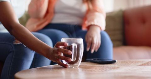 African american women reaching for steaming double-walled glass mug on wooden table in cozy living