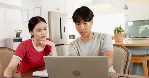 Asian Couple Collaborating at Home with Laptop and Notebook