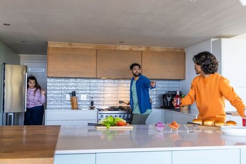 Diverse family preparing burgers on kitchen island, teen reaching for ketchup