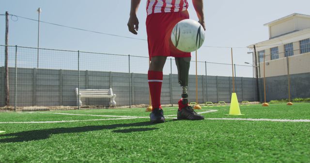 Midsection of disabled biracial male football player training on outdoor pitch. Football, sports, fitness, disability and inclusivity.