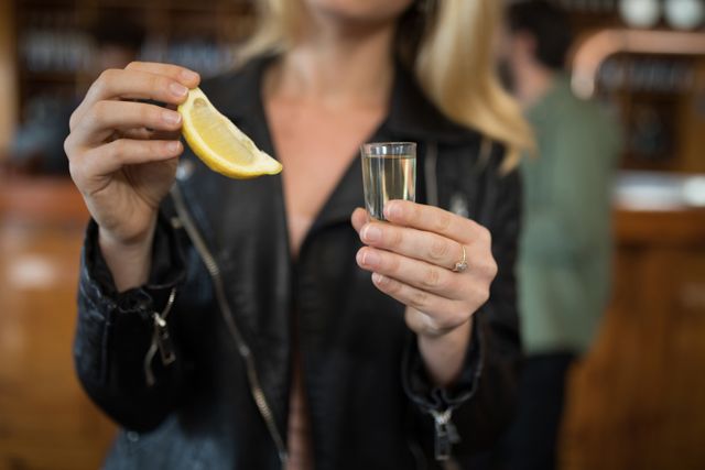 Mid section of woman holding tequila shot and lemon wedge in bar