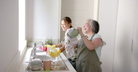 Asian Grandmother and Granddaughter Wash Dishes Together in Kitchen