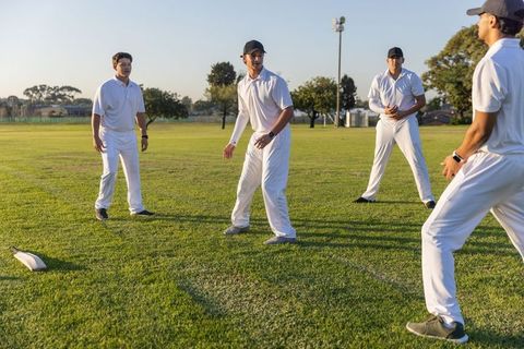 Young cricket team practicing fielding drills on sunlit park outfield wearing whites