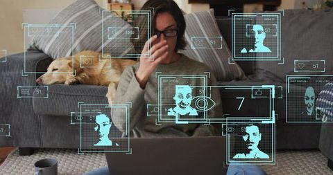 Woman using laptop with augmented reality facial recognition overlays in living room