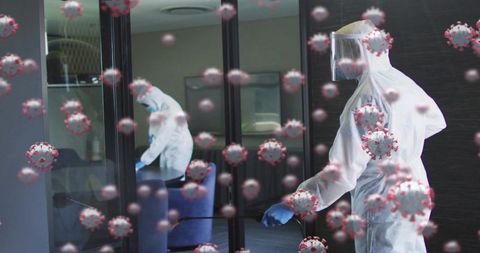 Worker in ppe disinfecting office lounge with sprayer and floating virus particles