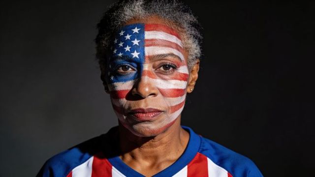 Senior woman wearing american flag face paint and sports jersey, dramatic lighting