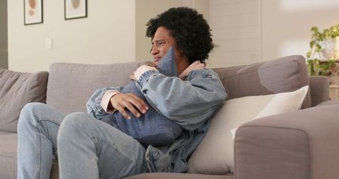 African american father cradling newborn wrapped in blue blanket on cozy gray sofa
