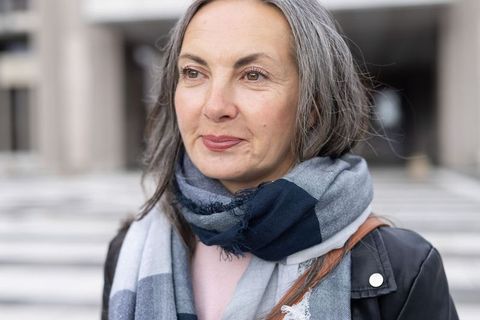 Mature gray-haired woman standing on urban steps wearing striped scarf and leather jacket