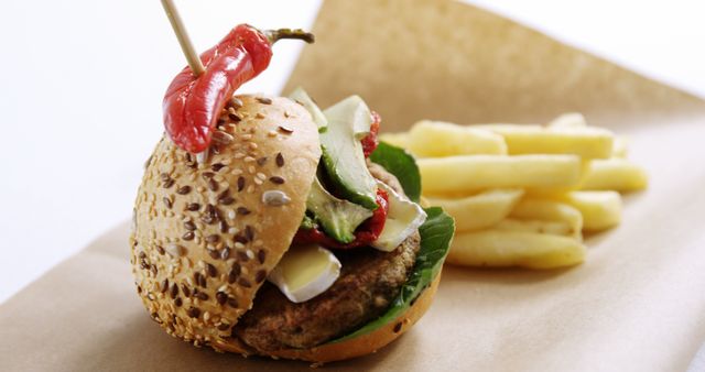 A delicious burger with sesame seeds on the bun, topped with a chili pepper and served with a side of fries, with copy space. Ideal for showcasing a gourmet fast food concept or a spicy meal option.