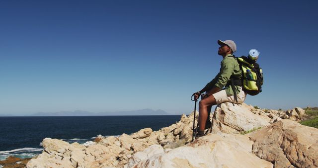 African american man hiking resting on a rock in countryside by the coast. fitness training and healthy outdoor lifestyle.