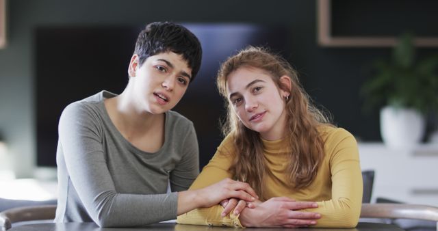 Two women sit together at a table, holding hands and showing mutual support and friendship. This image can be used for concepts like friendship, emotional support, connection, women's empowerment, mental health, and casual bonding moments. Suitable for use in blogs, articles on relationships, mental health awareness campaigns, or social media posts emphasizing support and compassion.
