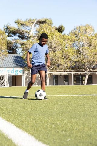 African american boy dribbling soccer ball on green turf school field practicing skills